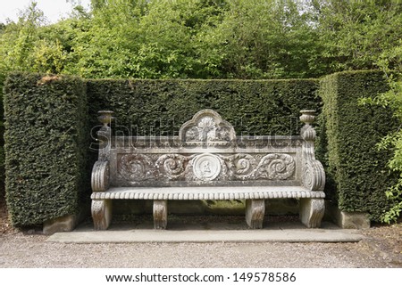 Ancient stone bench in a park surrounded by a high hedge