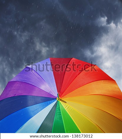 Rainbow umbrella on stormy sky background in heavy rain