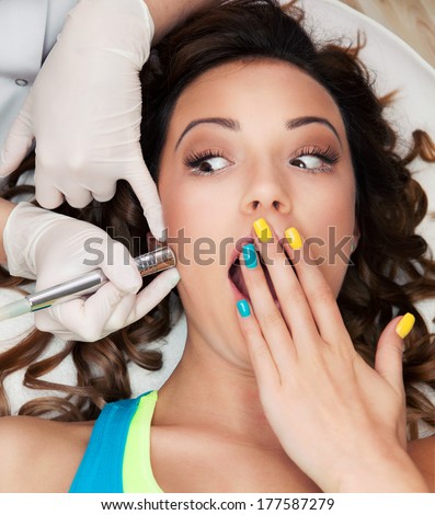Woman getting laser face treatment in medical spa center, hesitation, pain concept