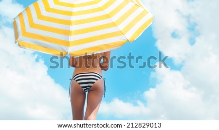 Sun protection and summer body care concept, woman wearing bikini under a beach umbrella