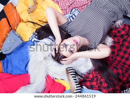 Nothing to wear concept, young attractive stressed woman lying down on a pile of clothes