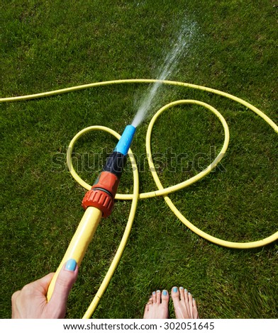 Woman\'s hand with garden hose watering grass, gardening concept