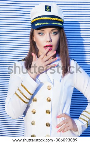 Surprised young attractive woman wearing marine captain uniform over stripy background
