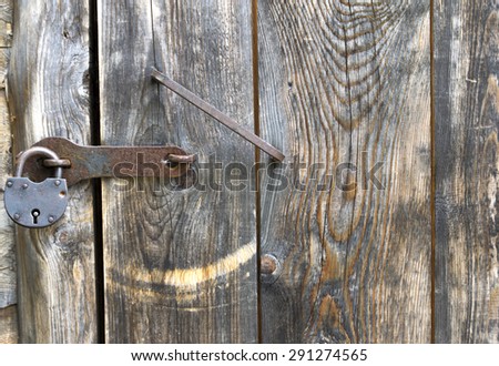 Ancient door with handle and padlocked barn. Dark tones and rust. The door is closed.