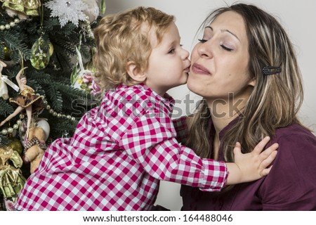 Son kisses his mother near Christmas tree
