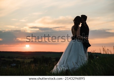 Silhouette of a wedding couple enjoying romantic moments at sunset. Bride and groom in field with sunlight. Newlyweds in nature location. Man and woman walking on meadow on top of mountain. Back view. Photo stock © 