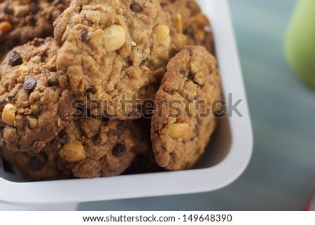 Home-baked chocolate chip cookies with macadamia nuts on white plastic plate with cup and scale in the background.