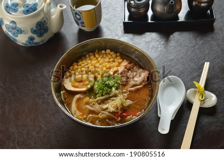 A bowl of Japanese ramen served with egg, sliced pork and bean sprout in spice soup on clean dark colored leather table top..