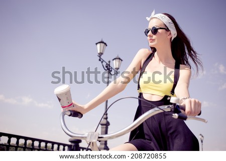 Portrait of a stylish girl hipster riding a cruiser bicycle with a disposable coffee cup