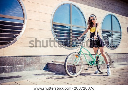 stylish girl hipster posing near cruiser bicycle against the background of the building with round windows