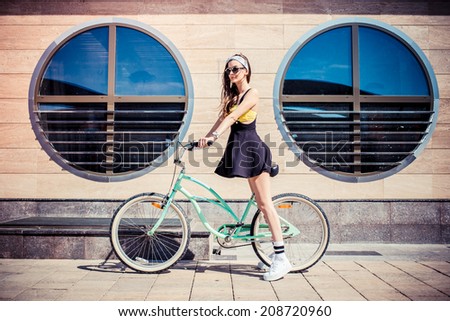 stylish girl hipster riding a  cruiser bicycle against the background of the building with round windows