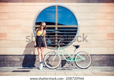 stylish girl hipster posing near cruiser bicycle against the background of the building with round windows