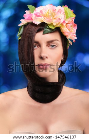 beautiful brunette girl wearing a wreath of pink tsetov with hair tied in a knot around the neck on a blue background with bokeh