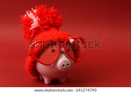 Piggy bank in love with red heart sunglasses with red hat and pom-pom standing on red background