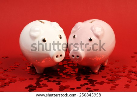 Two fallen in love piggies bank standing on red background with red shining heart glitters