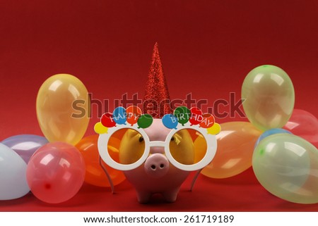 Piggy bank with sunglasses Happy birthday , party hat and multicolored party balloons on red background