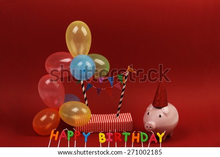 Piggy bank with sunglasses Happy birthday, party hat and multicolored party balloons on red background
