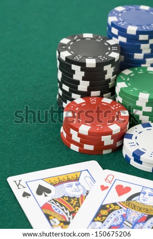 Closeup of queen of hearts and king of spades cards and poker chips on green felt surface