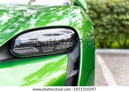 Close-up luxury shiny green sportscar supercar vehicle matrix LED system headlight lamp detail parked on city street outdoors. Electric car front bumper part