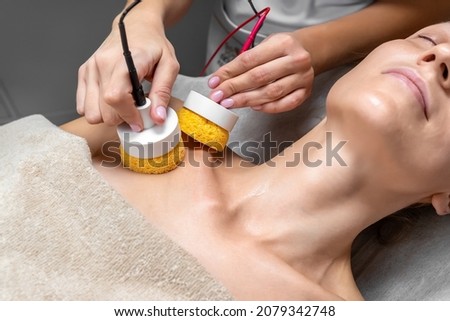 Close-up beautician doctor hand making anti-age face remodel procedure treatment with hardware microcurrent electric tool attractive young 30-40 female model at beauty clinic. Cosmetologist skincare Photo stock © 