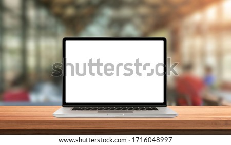 Laptop or notebook with blank screen on wood table in blurry background with coffee shop and nature green bokeh and sun light in morning.