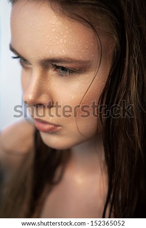 Close-up portrait of attractive young woman with beautiful face, wet hair and drops of water on her face, looking away
