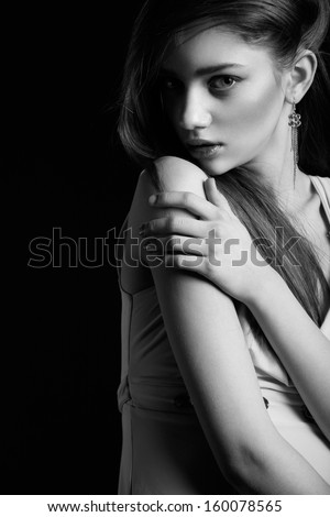 Waist up of pretty woman with beauty long hair, natural make-up and hugging herself, looking at camera. Black and White photo