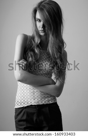 Waist up of pretty woman with beauty long hair, natural make-up and crossed hands,dressed in white T-shirt and dark grey shorts,  looking at camera. Black and White photo