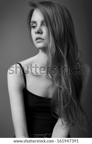 Sexy young woman with beautiful long hair and natural make-up, dressed in black top and looking away. Black and White portrait