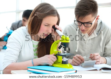 High School students concept. Group of excited students working  with microscope discovering  a biological sample in science classroom