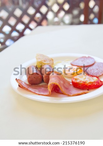 breakfast with fried eggs, bacon, sausages, tomato and salami