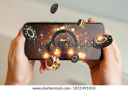 Creative background, online casino, in a man's hand a smartphone with playing cards, roulette and chips, black-gold background. Internet gambling concept. Copy space.