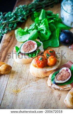 Appetizer sandwiches with figs, prosciutto, arugula, goat cheese, tomatoes and garlic