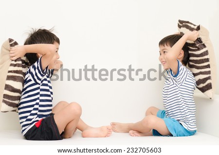 Little sibling boy playing pillow fighting on sofa