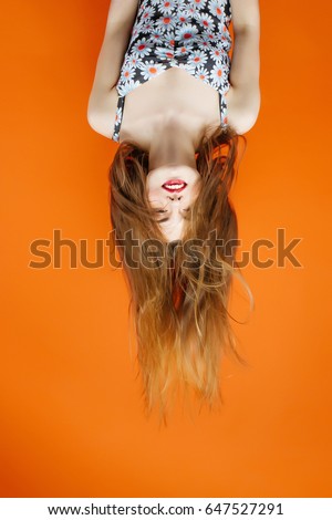 Portrait of Brunette with Long Dark Hair Wearing Dress with Flowers Upside Down in Studio on Orange Background. Hair Style Concept. 商業照片 © 