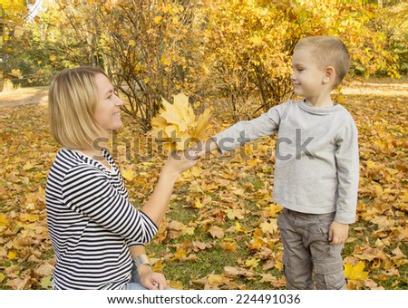 handsome boy presents to his mother autumn leaves in the park