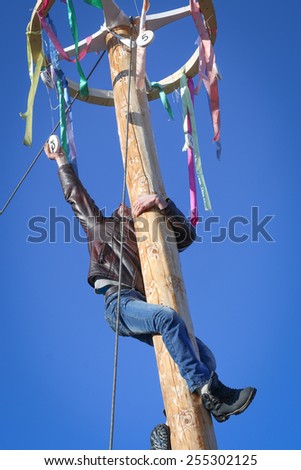 Man climbing the pole for prize during winter carnival Maslenitsa in Russia