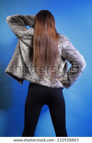 young fashionable woman in fur coat long hair back view blue background