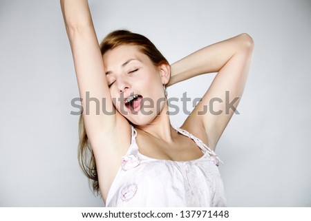 Attractive blonde woman with no make up yawning and stretching gray background