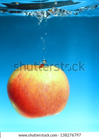 Yellow red apple in the water splash over blue background. Healthy food and active life. Square format