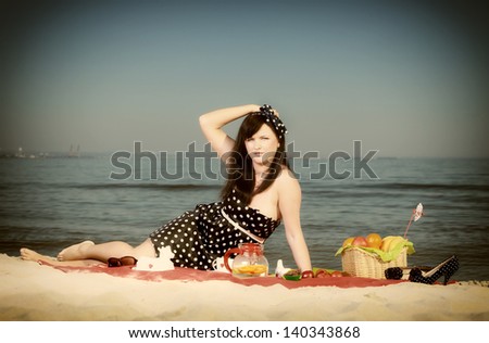 Picnic outdoors. Beautiful woman sitting on red blanket on sandy beach. Retro style.