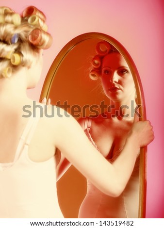 Sexy woman preparing to party, girl in underwear with curlers in hair looking at the mirror pink background