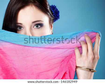 Young woman make up on eyes hides her face with multicolored shawl blue background