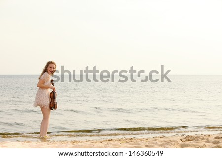 Happy crazy blonde girl music lover on beach with a violin. Love of music concept.