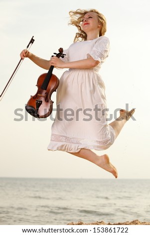Happy crazy blonde girl music lover on beach jumping with a violin. Love of music concept.
