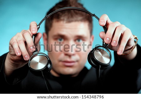 music and technology - young smiling man offering headphones on blue background