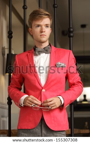 Young handsome stylish man fashion model wearing bright red jacket and bow tie posing indoor