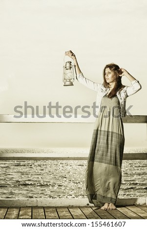 Sepia photo. Full length young woman on pier with a oil kerosene lamp. Concept carrying light, daylight