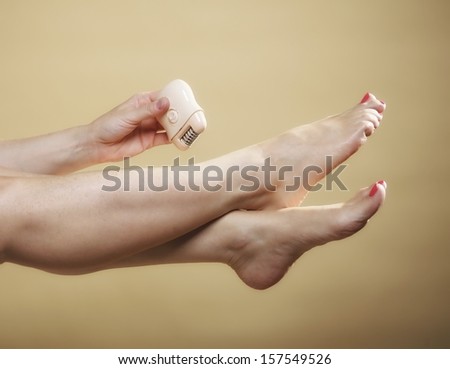 woman shaving her legs with electric shaver depilation body care on orange. Beauty and skin care concept.