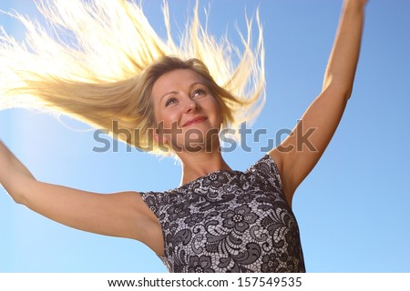 young woman smiling blonde girl wind in hair outstretched arms blue sky background, happiness freedom concept